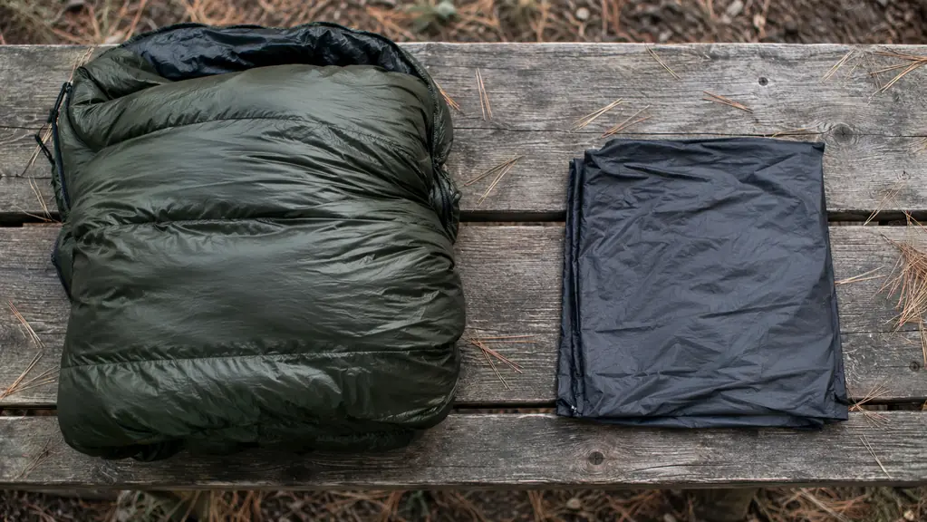 A thick insulated sleeping bag and a thin folded fabric liner laid side by side on a picnic table